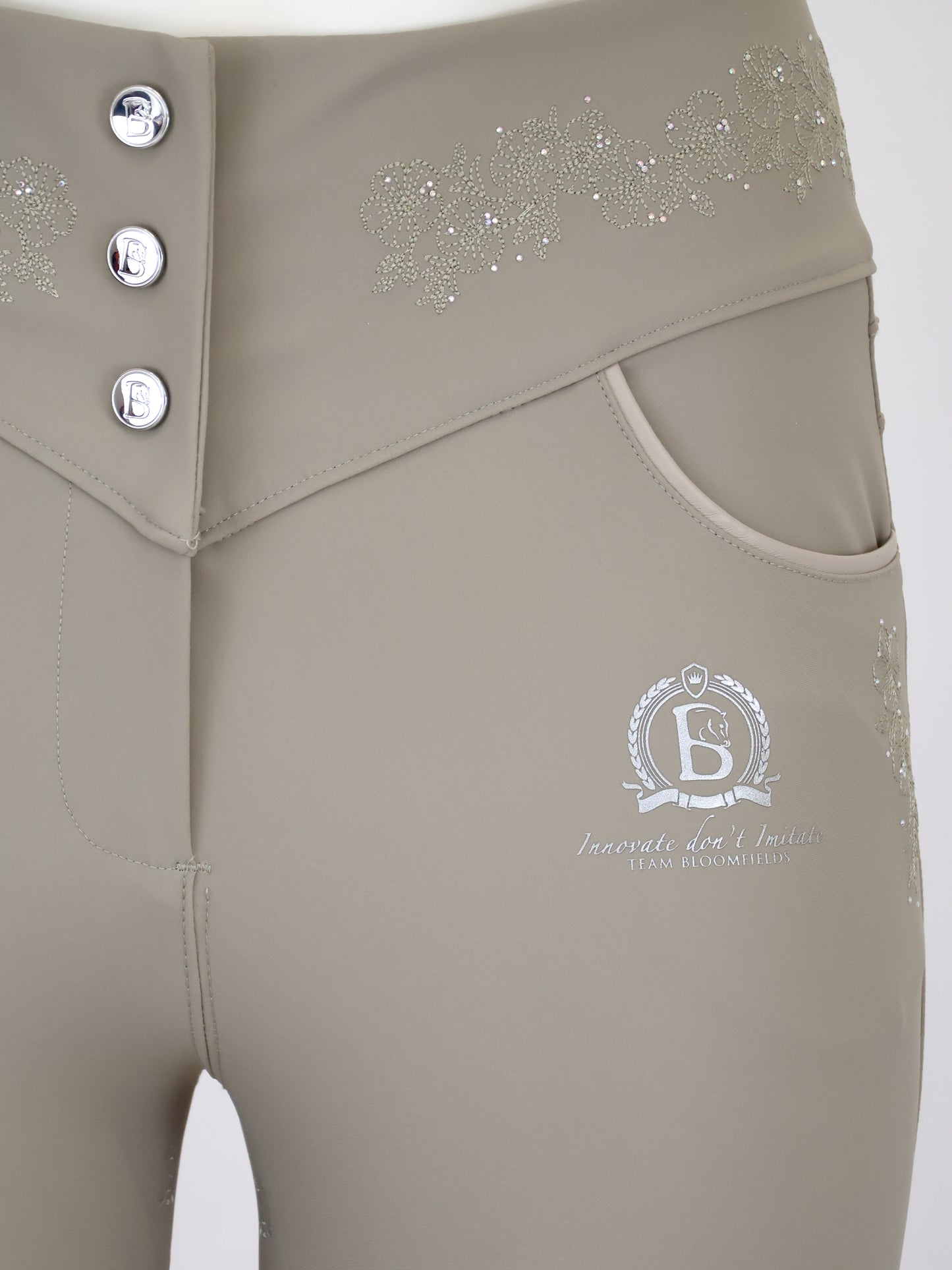 Close-up of a pair of beige riding breeches featuring a three-button waistband, side pockets, and silver rhinestone embellishments on the hip.
