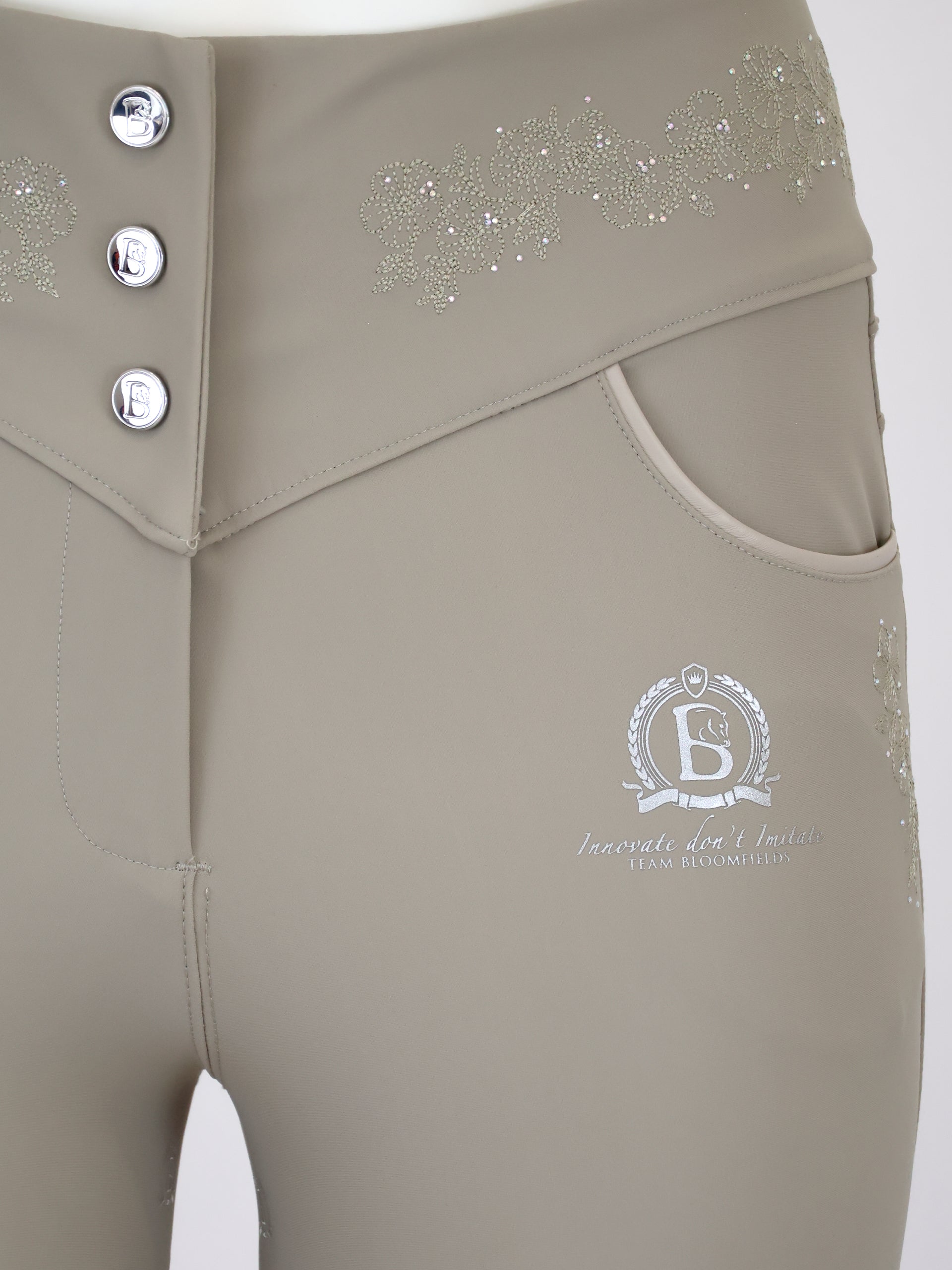 Close-up of a pair of beige riding breeches featuring a three-button waistband, side pockets, and silver rhinestone embellishments on the hip.